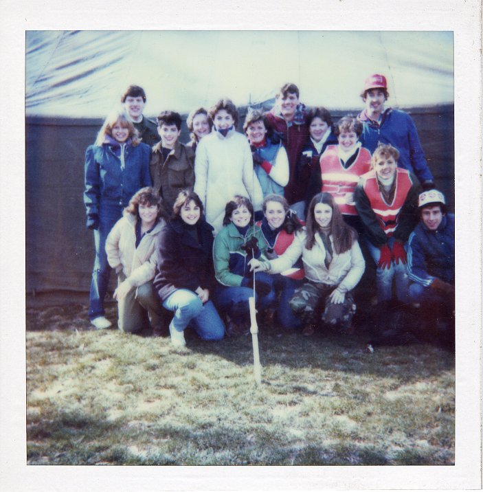 This photo is of 17 people posing in front of a large tent which is is located on a grassy lawn on the Mary Washington campus. 
