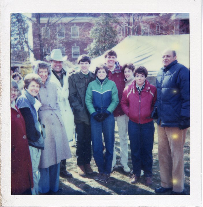 A photo of 10 people who are posing on a grassy lawn on the Mary Washington campus. There are a few people in the background as well as a large tent. 