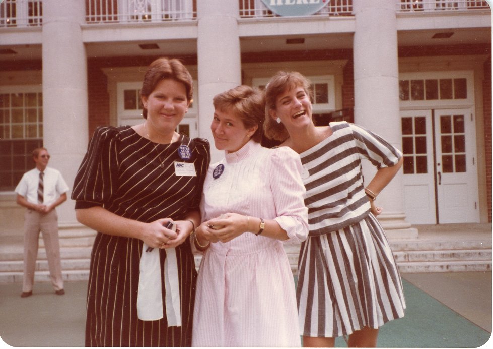 This image features three young women standing, posing for the picture, in front of a large brick building with white columns and multiple sets of double doors. 
