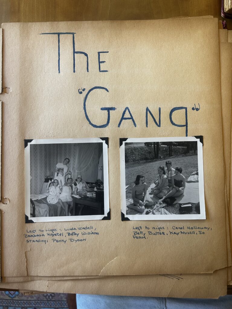 This vintage scrapbook page, titled "The 'Gang'" in stylized blue lettering, features two black-and-white photographs of young women in the mid-20th century. Below the photos, hand-written captions identify the friends posing indoors and outdoors on a grassy lawn.