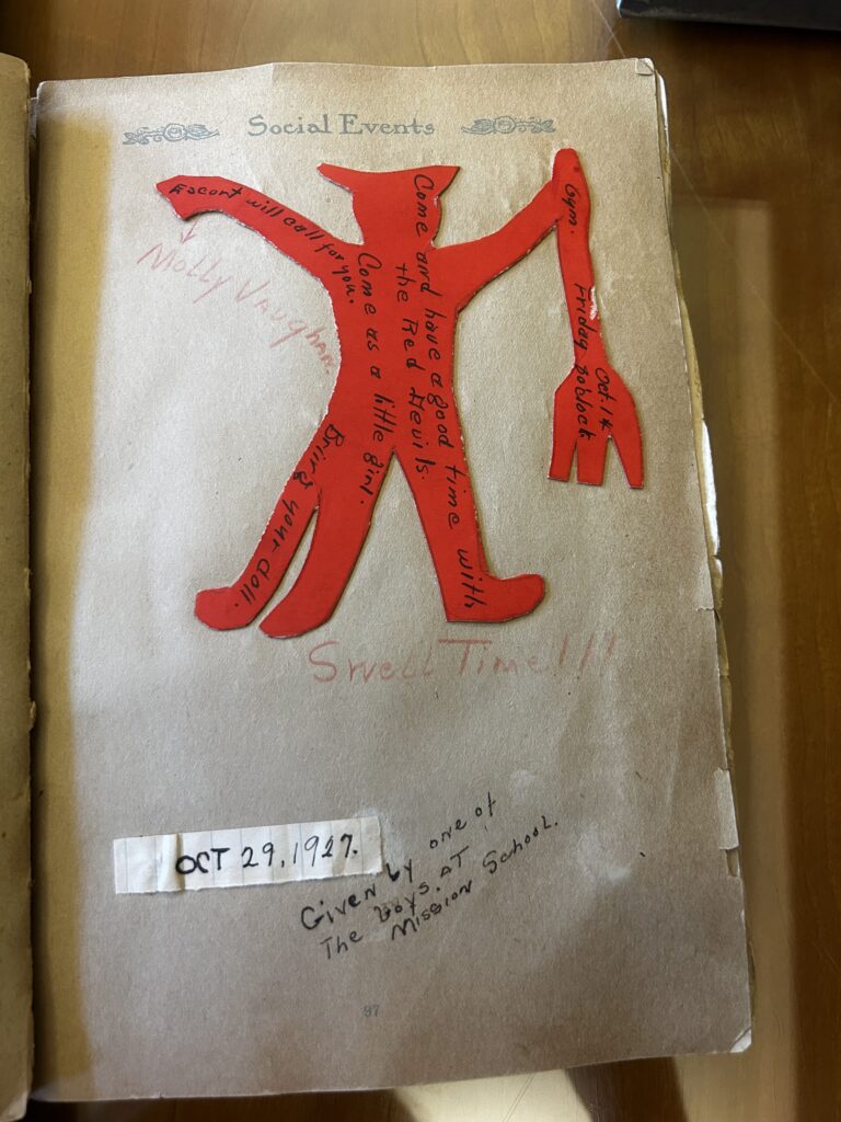 This "Social Events" scrapbook page features a bright red, hand-cut paper devil figure glued to the center, which serves as a whimsical invitation to "come and have a good time with the Red Devils." Hand-lettered notes on and around the figure mention a date of October 29, 1927, and indicate the event was hosted by "one of the boys at the Mission School."