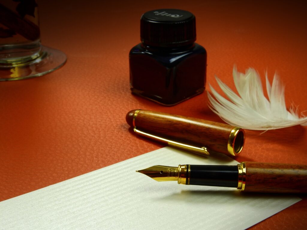 This image shows a fountain pen open over top of a piece of paper. The pen and paper look to be on top of an orange surface.