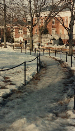This image depicts a roped-off pathway leading to a large brick building. The scene is covered in a thin layer of ice and snow. 